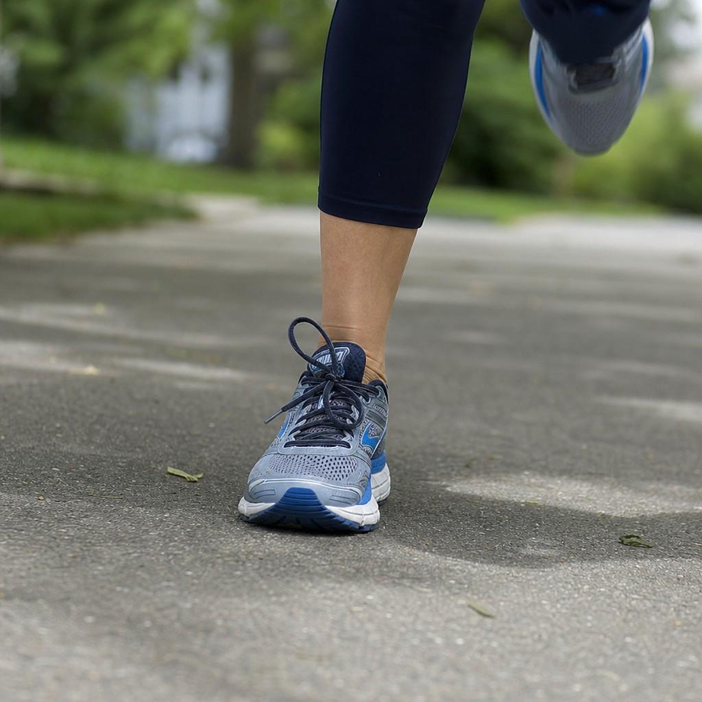 Close-up of a woman's running shoes mid-stride striking a paved suburban path