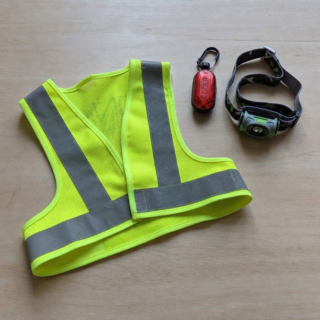 Reflective running gear laid flat: a hi-vis vest, a clip-on red rear light, and a headlamp