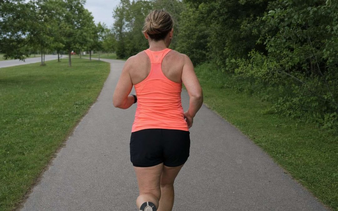 A woman running along a park path seen from behind in a bright coral technical top