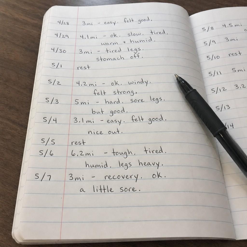 Close-up of a handwritten running log open on a table showing dates and brief notes in everyday handwriting
